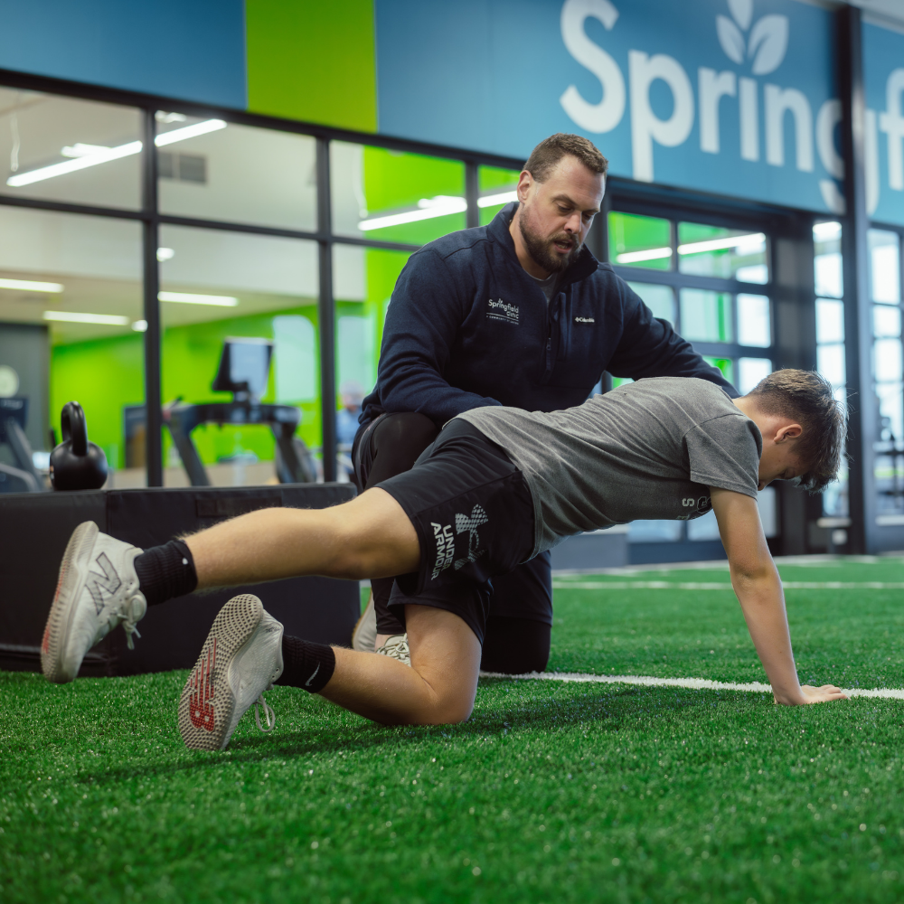 Male personal trainer with youth athlete in well-lit fitness center