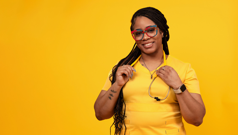 Female wearing yellow scrubs and glasses smiling in front of yellow photo backdrop