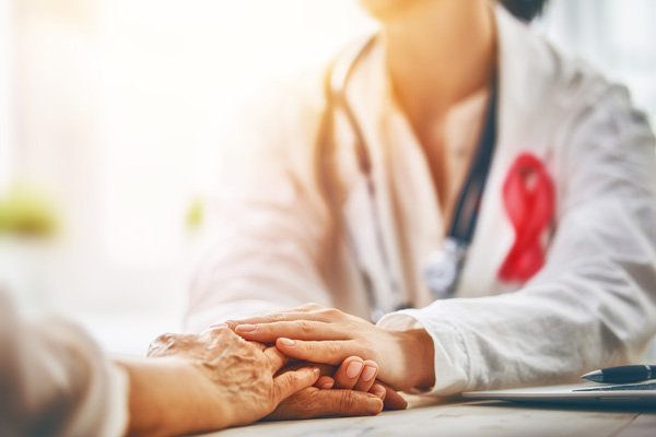 Doctor wearing white medical coat and pink cancer ribbon comforting the hands of a patient