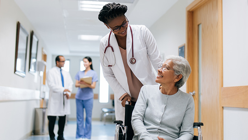 Elderly patient getting walked in wheelchair by medical professional in hospital setting