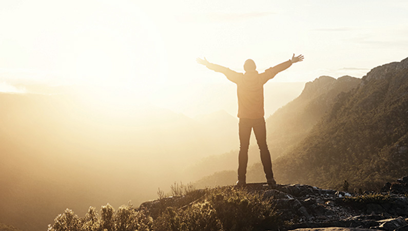 Individual with arms spread out looking out on top of a hill at sunset