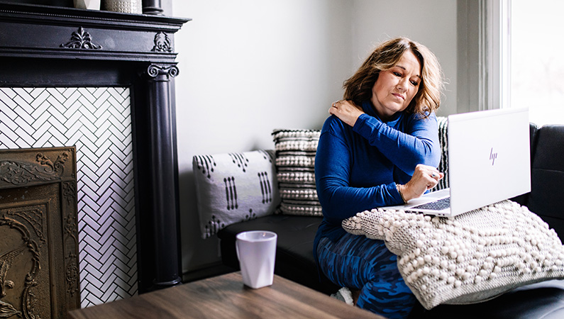 Woman working from home on laptop grabbing shoulder in pain