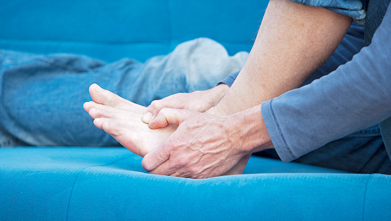 Older male gripping his foot while sitting down on blue couch