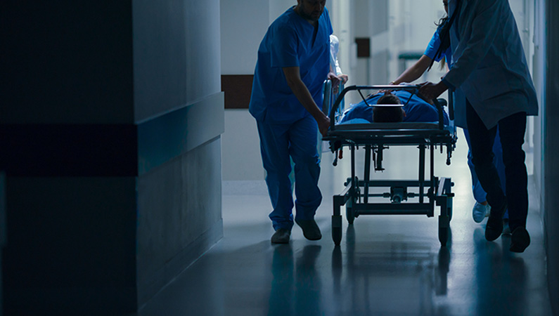 Medical specialists in dark hallway of hospital quickly pushing patient on stretcher