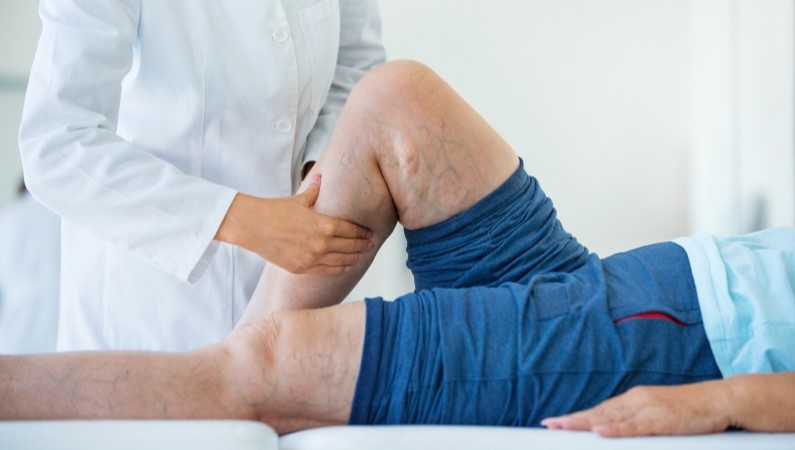 Doctor examining patient's leg while patient lays on exam table.