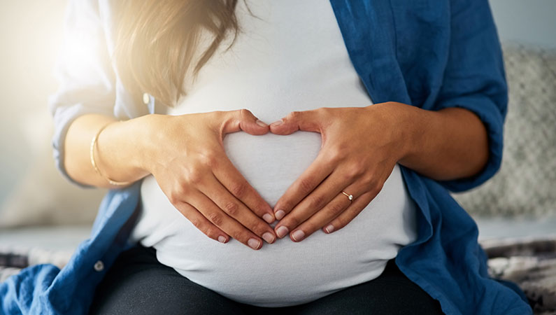 Woman making a heart with her hands on her pregnant stomach