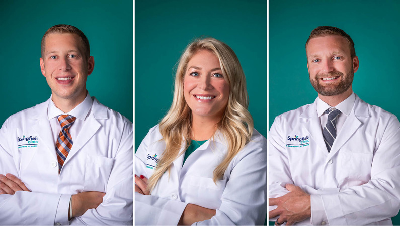 Three medical professionals wearing white medical coats smiling on green background