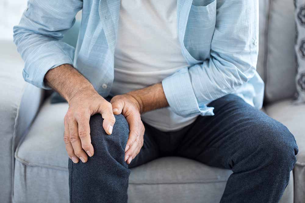 Man in jeans sitting down holding knee in pain.