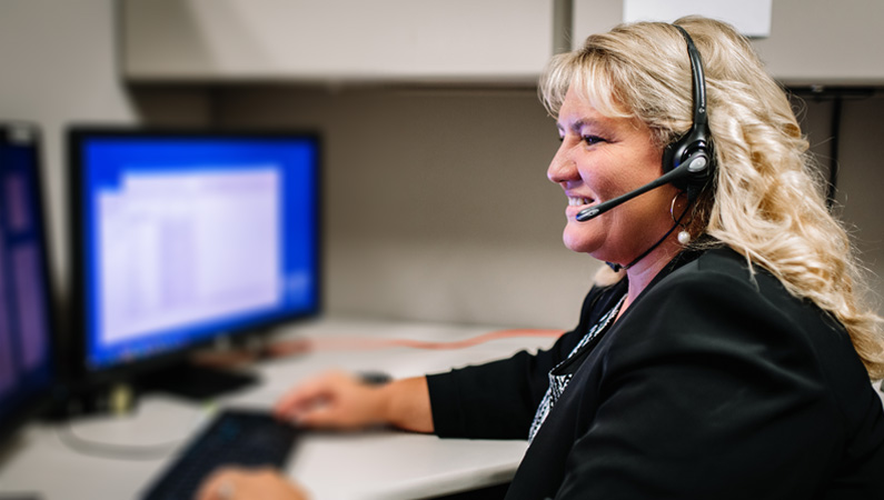 Female wearing microphone headset smiling while working on the computer.
