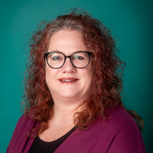 Professional headshot of female with curly red hair and glasses