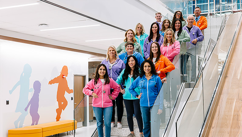 Group of pediatric doctors and nurses wearing colorful jackets standing on stairs inside a Pediatric medical facility.