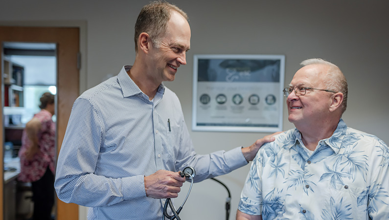 Male doctor smiling with patient in patient exam room.