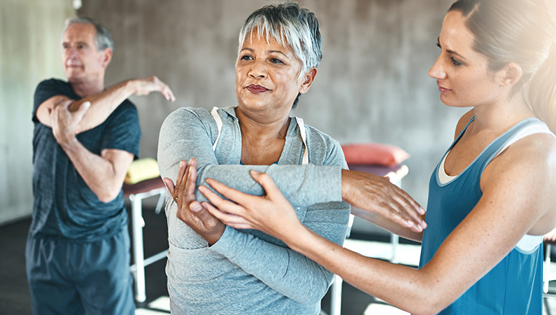 Younger female in workout clothes stretching out older female