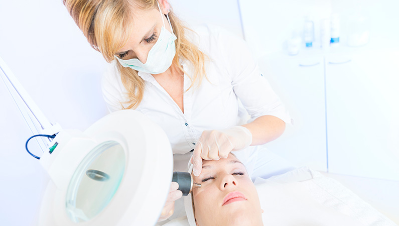 Female in exam room with eyes closed getting cosmetic medical services performed on face