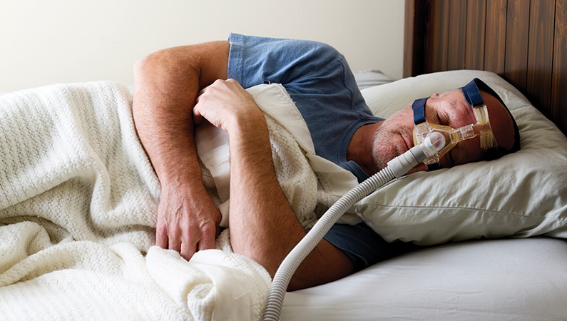 Male sleeping in a bed with the assistance of a CPAP machine.
