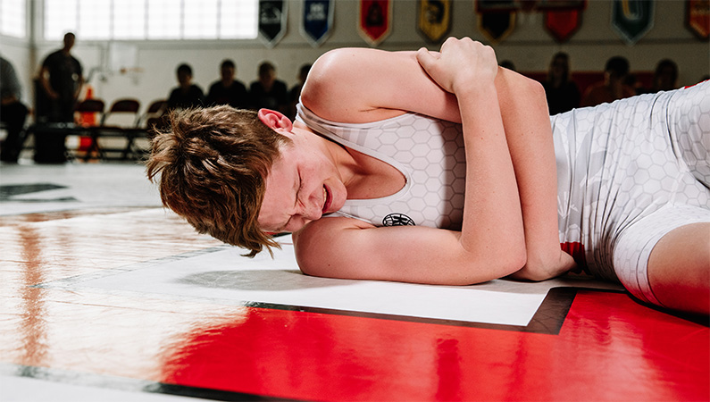 Male wrestling athlete laying on mat holding shoulder in pain