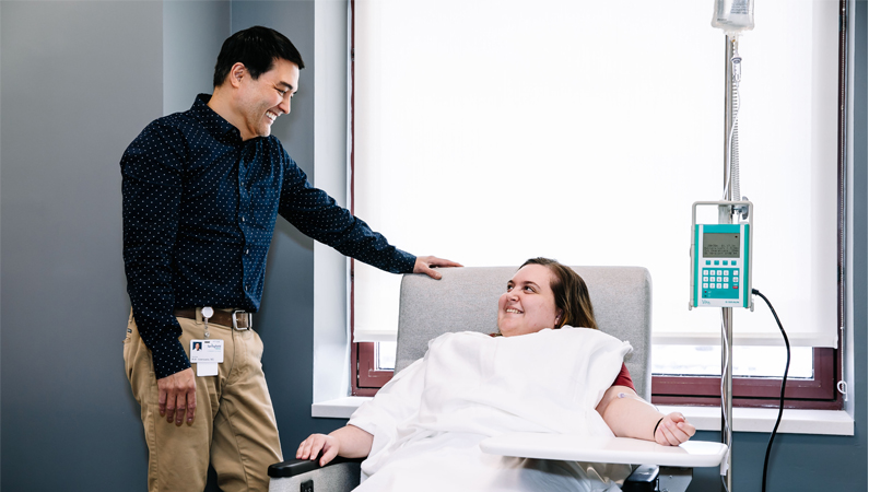 Neurology doctor smiling at a patient seated in an infusion chair receiving treatment.