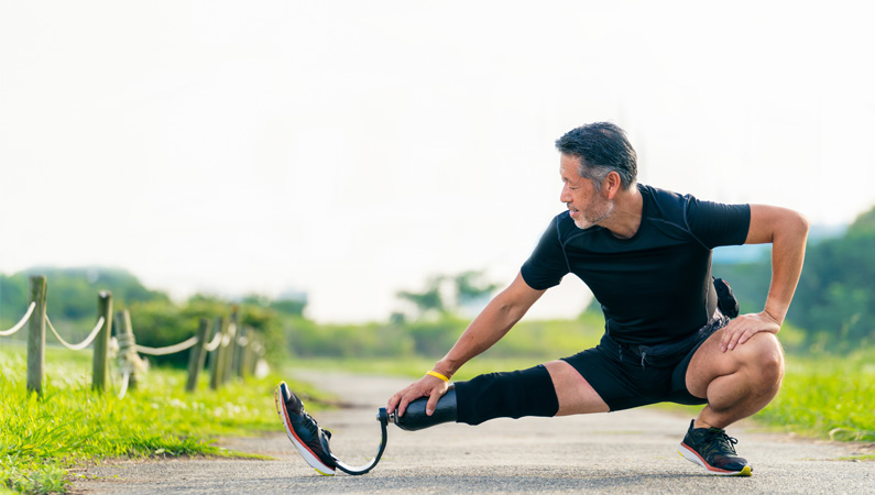 Man with prosthetic leg in athletic wear stretching outside.