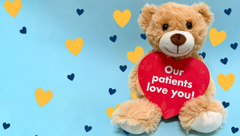 Stuffed teddy bear holding red heart sign that reads "Our patients love you!"