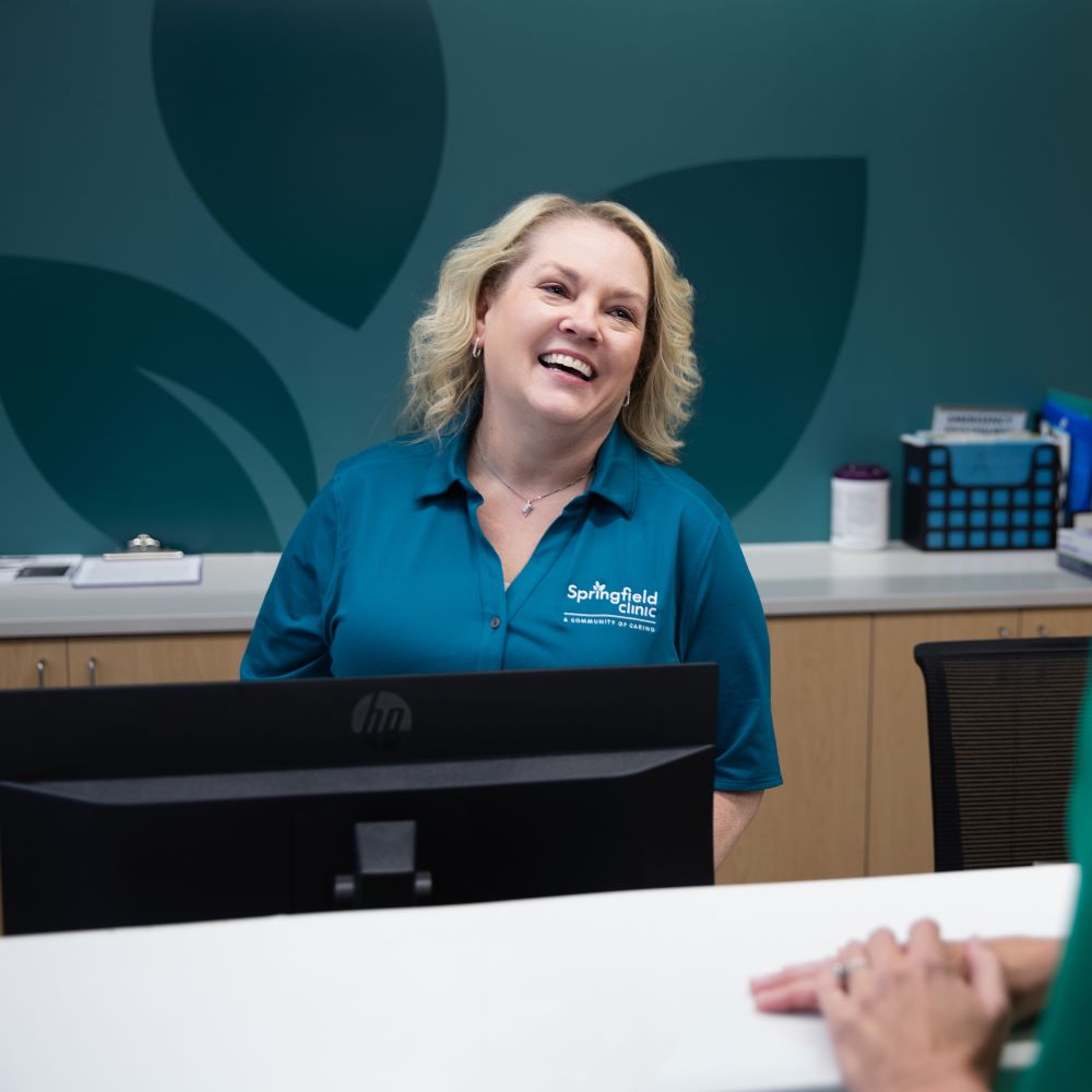 Patient Access Specialist with Springfield Clinic smiling behind receptionist desk.