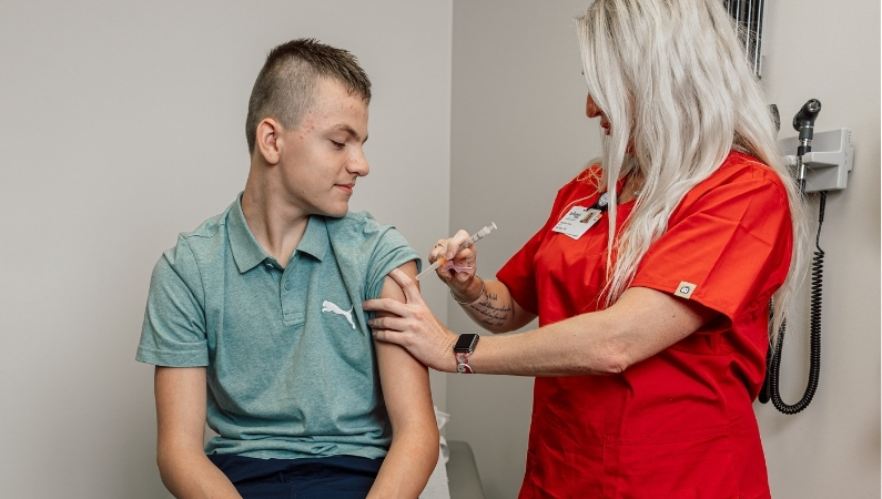 Clinical staff providing shot to older child patient in exam room