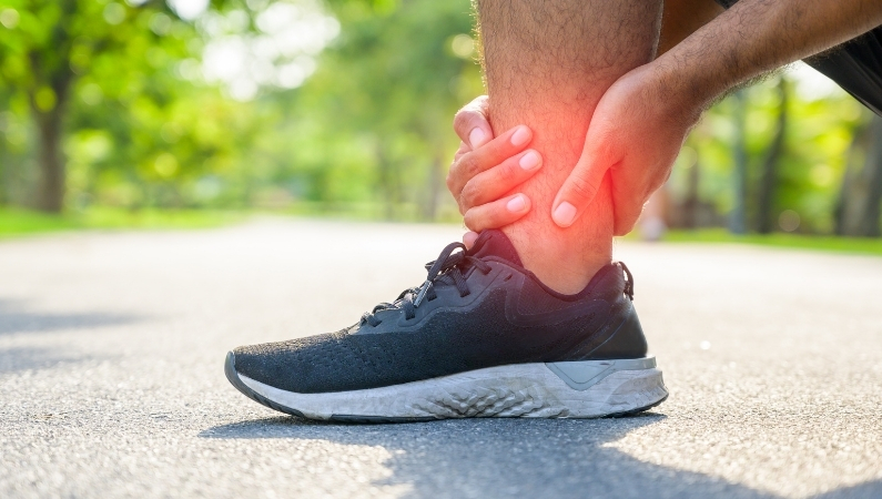 Foot with athletic shoe on pavement outside with red areas indicating pain on foot and ankle.