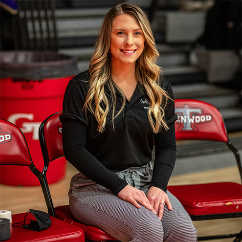 Female athletic trainer sitting in a chair smiling in school gym.