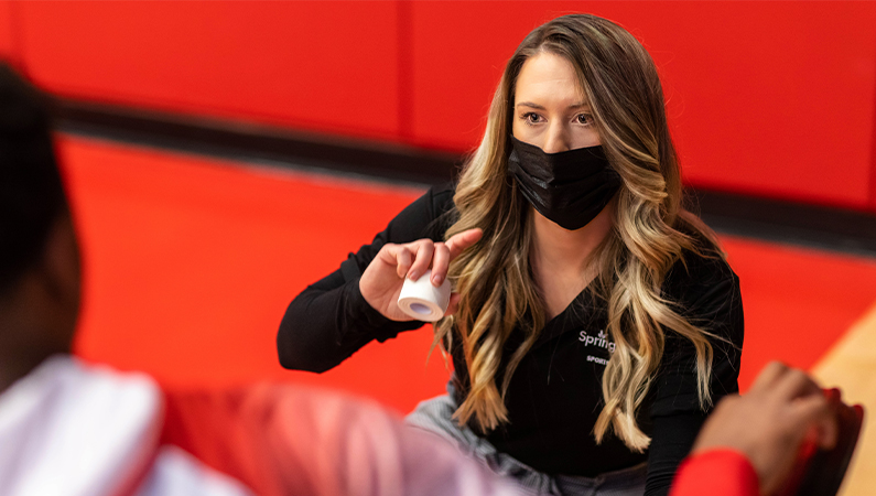 Female athletic trainer with a medical mask on talking to an athlete.