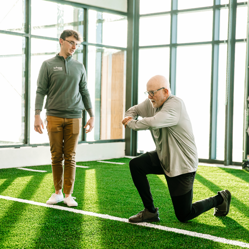 Male personal trainer with man in well-lit fitness center