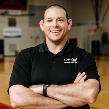 Male athletic trainer smiling in school gym setting.