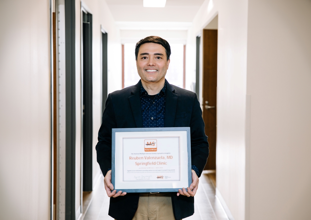 Male neurologist smiling holding a plaque award.