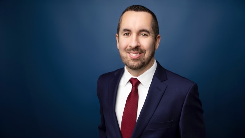 Ryan Caldwell smiling in front of blue photo backdrop.