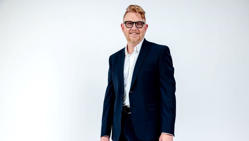 Male women's health physician smiling in front of a white photo backdrop.