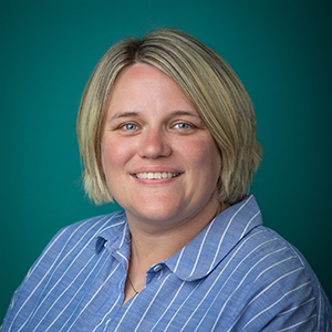 Female physical therapist smiling in front of blue photo backdrop.