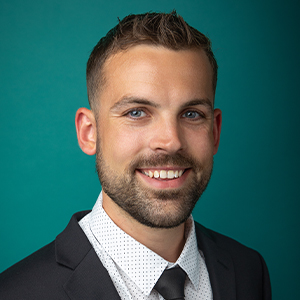 Male physical therapist smiling in front of blue photo backdrop.