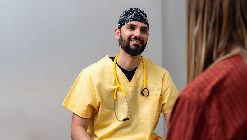 Male wearing yellow scrubs smiling in patient room