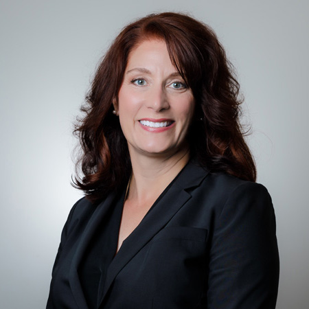 Female chiropractic doctor smiling in black blazer in front of a white gradient backdrop.
