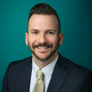 Male physical therapist smiling in front of green photo backdrop.