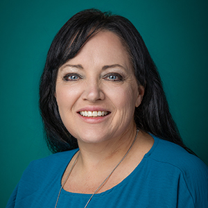 Female nurse practitioner smiling in front of green photo backdrop.