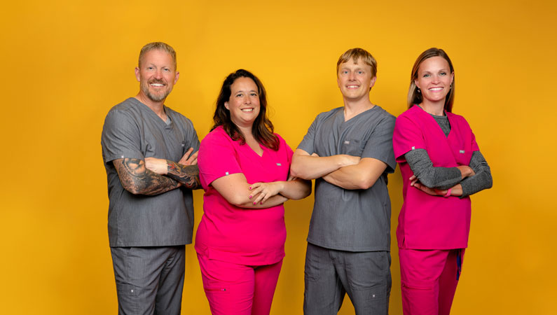 Four pediatricians in scrubs posing in front of a yellow background