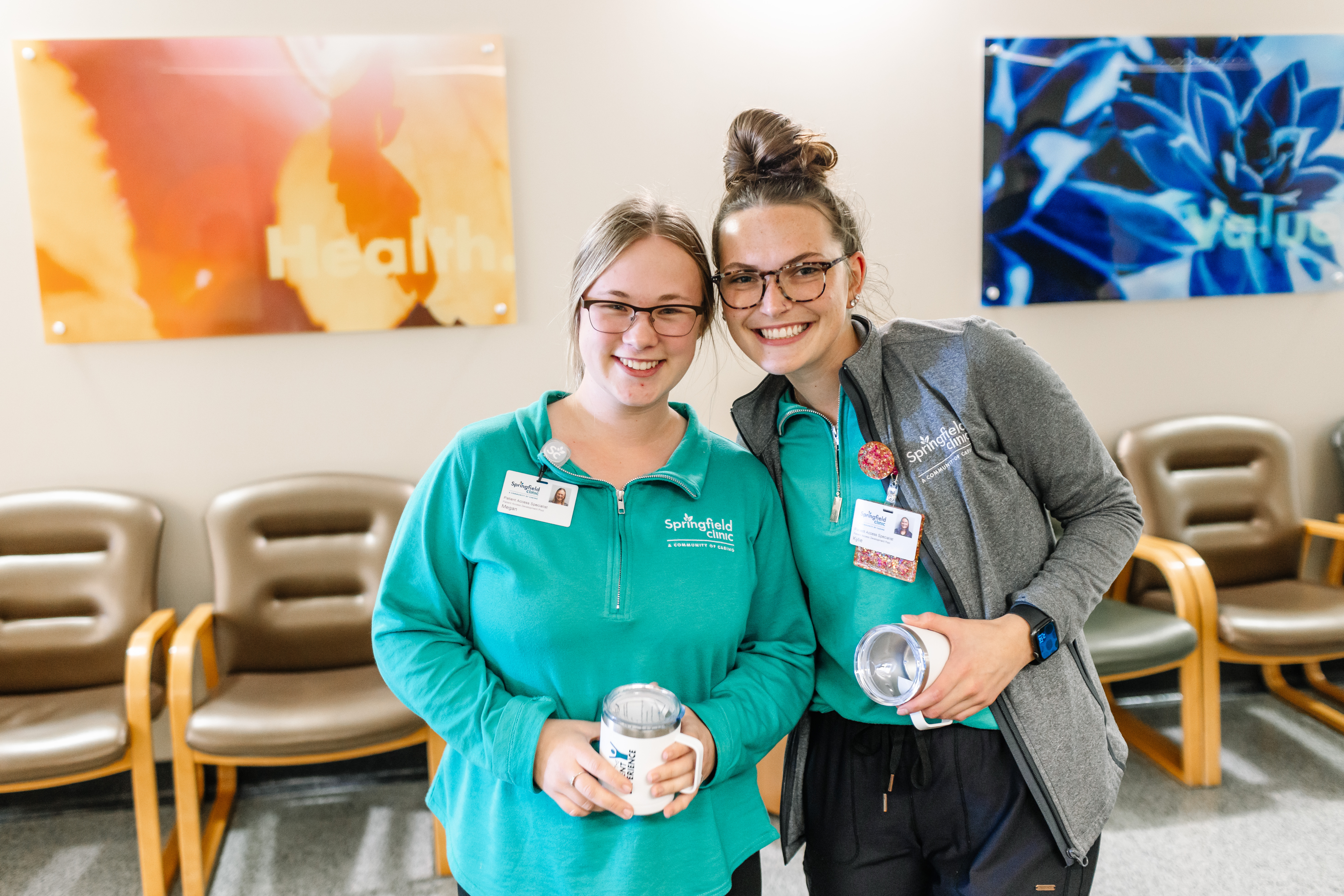 Two Springfield Clinic employees smile while holding their I Am The Patient Experience Mugs they were awarded for exceptional work.