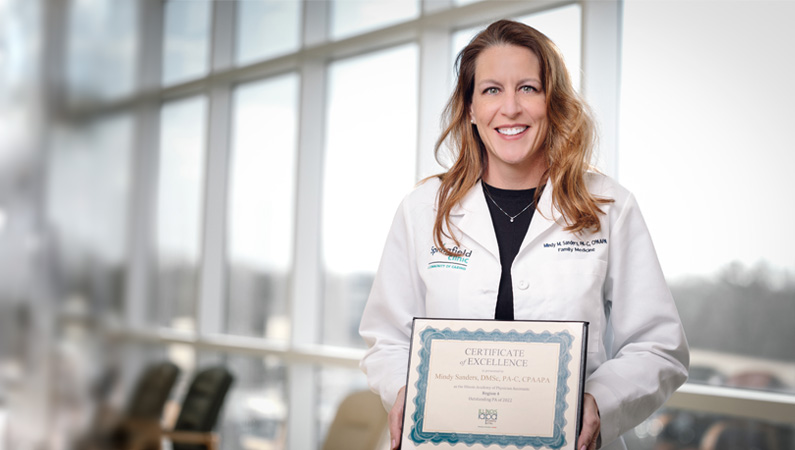 Female physician assistant holding award in outdoor setting.