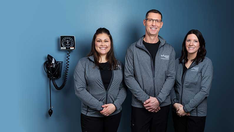 Group of three medical professionals smiling in exam room