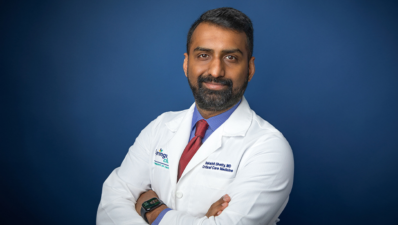 Male trauma surgeon smiling in front of blue photo backdrop