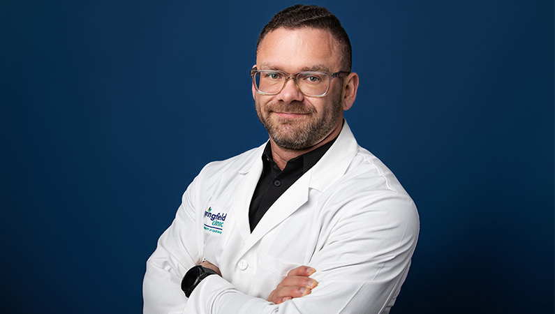 Doctor wearing white medical coat smiling in front of blue background
