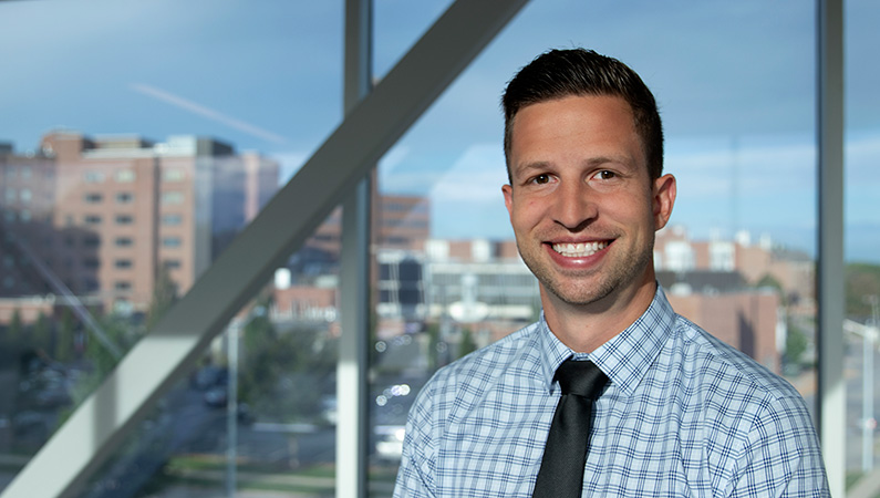 Man smiling in front of window with hospital buildings in view.