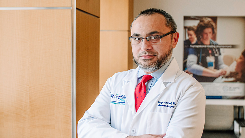 Male wearing glasses and white medical coat with red tie posing in office setting