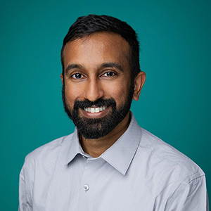 Male cardiologist smiling in front of green photo backdrop.