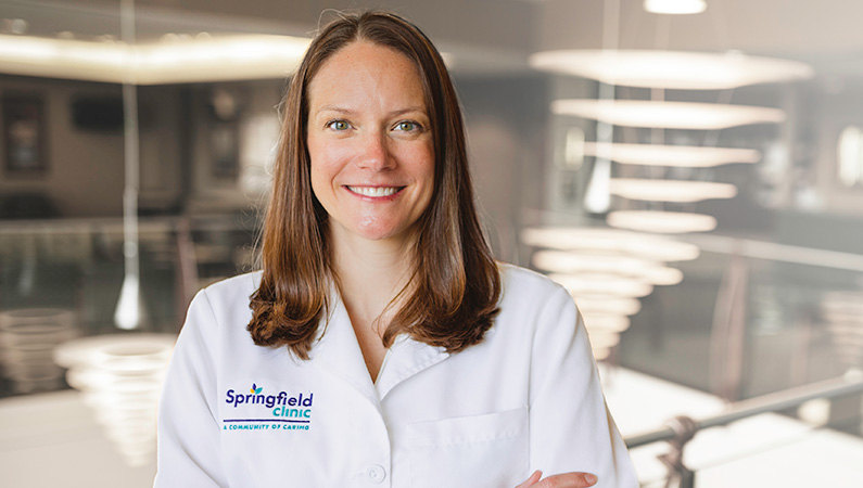 Woman wearing white doctors coat, smiling in well lit lobby.
