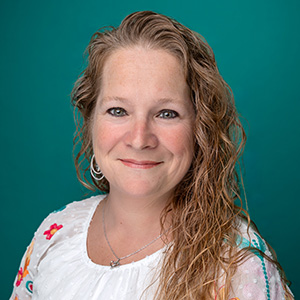 Female nurse practitioner smiling in front of teal blue backdrop.